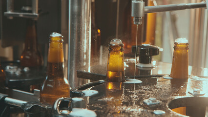 Industrial bottling machine filling brown beer bottles with golden alcoholic craft beverage, creating foam overflow on the production line at a modern brewery plant