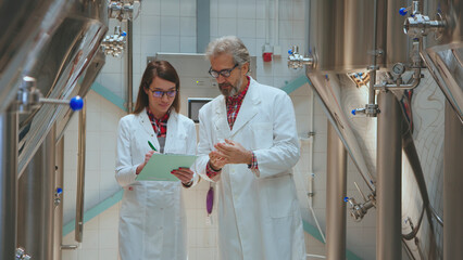 Brewery quality control team members wearing lab coats, collaborating and inspecting samples in a...