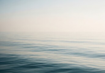 Obraz premium Calm sea under a hazy sky, with gentle ripples on the waters surface creating subtle patterns and a serene, tranquil atmosphere