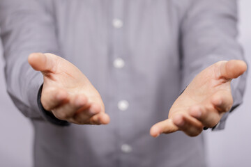 Obraz premium A close-up shot shows a person offering their open hands. The man is wearing a grey shirt and the background is blurred, suggesting generosity,