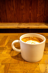 Hot latte, coffee with milk, and foam art on top in white ceramic cup on wooden table, in warm mood