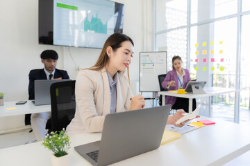 Company employees are working in the office. Asian marketing team is analyzing website design on computer screen.