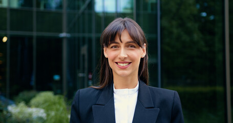 Close-up of a young woman posing for the camera and smiling, standing outdoors in front of modern...