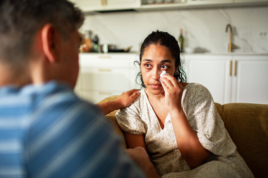 Young woman crying with support from her husband at home