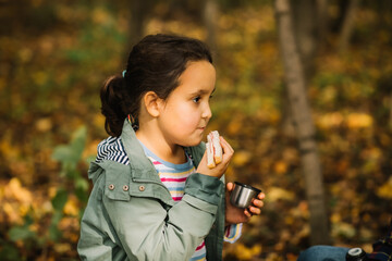 Little kid girl hiking in the forest with family relax sitting on stump and drinks from thermos