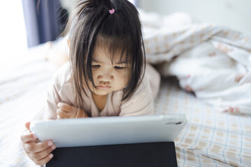 Cute little Asian girl is sleeping on the bed with a tablet,Little asian girl playing with a digital tablet on bed room,A little Asian girl is lying on the bed watching a tablet.