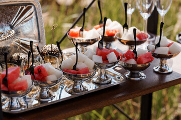 Elegant Outdoor Fruit Dessert Presentation with Watermelon, Radishes, Silverware, and Glass Bowls on a Dark Wooden Table.