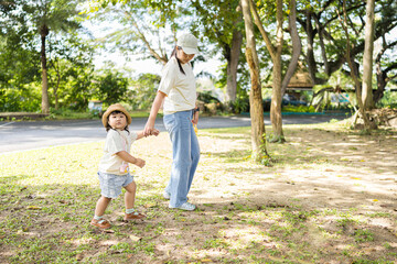 Fototapeta premium A mother is holding hands with her cute little Asian daughter as they walk in a park on a weekend,Mother walking and holding hands with daughter for bonding, outdoor adventure or journey in nature. 