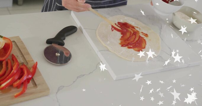 Boy in apron spreading tomato sauce on dough in home kitchen, with pepper strips and cheese - Powered by Adobe