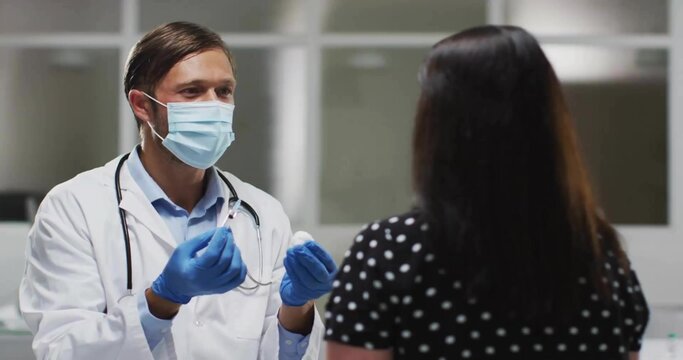 Demonstrating doctor wearing lab coat and mask preparing injection in clinic with vial, copy space