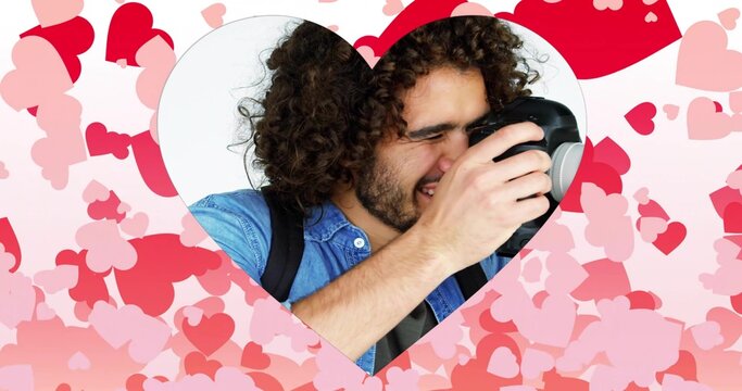 Male photographer holding DSLR up to eye inside heart cutout overlay at studio backdrop, with strap - Powered by Adobe