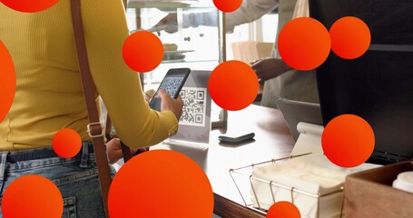 Using smartphone woman wearing yellow top scanning QR code sign at cafe counter, with card reader