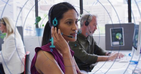 Adjusting headset microphone, woman in purple blouse sitting at white desk with computers in office