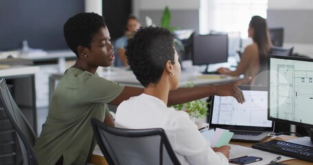 Two women collaborating on design review in open office, with dual monitors and color swatches