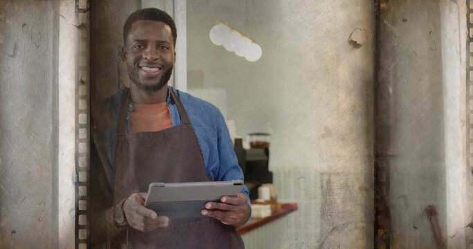 Smiling barista wearing brown apron holding tablet at coffee shop entrance, with coffee machine