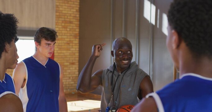 Standing senior coach addressing players at high school gym court, with basketball and whistle