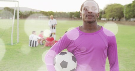Naklejka premium Standing soccer goalkeeper wearing purple jersey holding ball on grass field, copy space