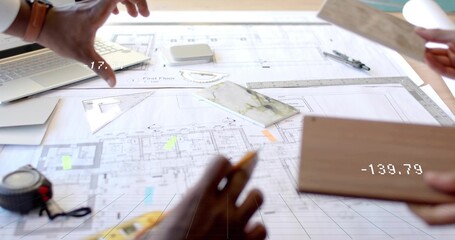 Architects examining floor plan blueprint in design studio, with laptop and tile samples