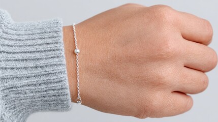 Female hand wearing delicate silver chain bracelet with small bead, cozy winter outfit and minimal jewelry style