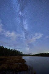 Milky way and clouds over the forest lake
