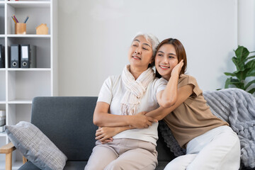 Smiling Asian mother and young daughter bonding on a sofa, representing generations of family love and happiness at home