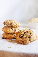 A freshly baked oatmeal raisin cookie with visible oats placed on natural linen tablecloth background.