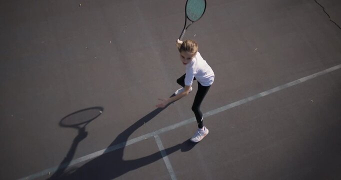 A young girl intensely focused on a tennis game, hitting a forehand on a sunlit outdoor court. This image captures the essence of youth sports and dedication.