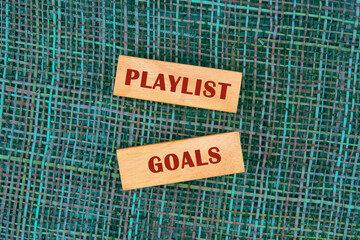 Two wooden blocks display the words playlist and goals, resting on a vibrant woven surface. The image inspires creativity for crafting the perfect music collection