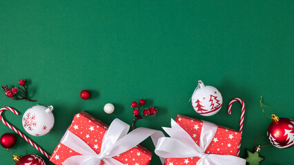 Flat lay Christmas composition with red gifts, ornaments, and candy canes on a green background. Festive mood in red and white tones, symbolizing holiday joy and winter magic.