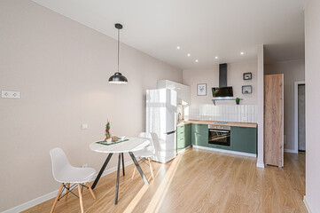A bright, modern kitchen and dining area featuring a white round table, chairs, and green cabinets. Clean lines and neutral tones create a welcoming space