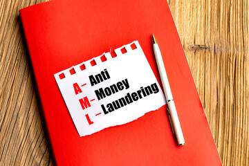 Anti money laundering acronym AML on torn paper with pen and red notebook on wooden desk