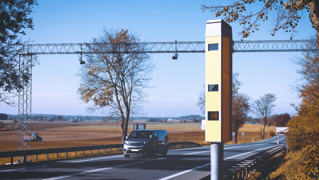 A speed camera at the roadside with a car passing by in the background.