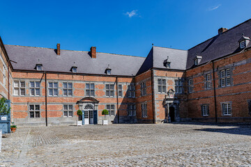 Entrance courtyard at Freyr Castle with Renaissance-style building, cobblestone floor, brick walls, multiple windows, two entrance doors and gable roof, sunny summer day in Namur, Wallonia, Belgium