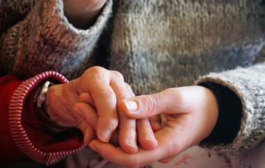 Sitzende jugendliche Enkeltochter mit grauer Strickjacke hält Hand von alter Großmutter 