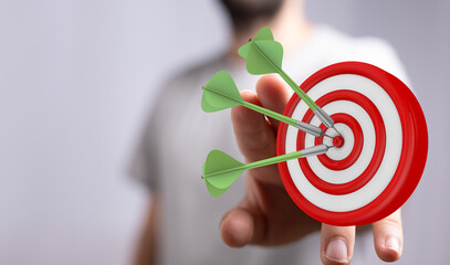 Close up of a person's hand holding a dartboard with three darts hitting the center, symbolizing...