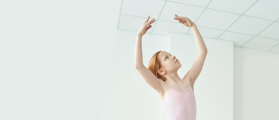 Young caucasian female ballerina practicing dance poses in bright studio setting.