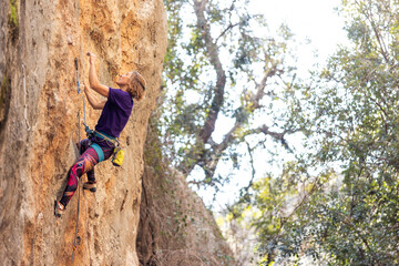 woman climbing steep wall of rocky mountain. Girl climber overcomes challenging route.