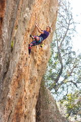 A woman climbs a rock, a strong girl trains strength and endurance, extreme sport, rock climbing on natural terrain, a rock climber climbs.