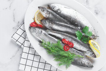Fresh Herring fish, ready to cook, with herbs and spices, on a white platter, in the kitchen