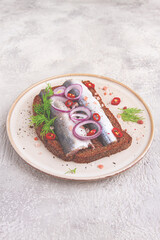 sandwiches , Herring fish, on dark rye bread, sprinkled with onion, chili pepper and herbs, on a light plate
