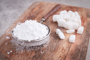 a strainer with powdered sugar, on a wooden cutting board, with pieces of white sugar,