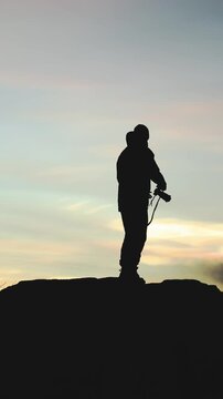 Man steps onto a rocky ledge and photographs nacreous, polar stratospheric clouds in Arctic Norway