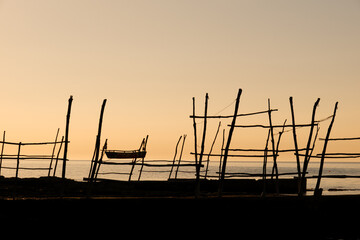 Silhouette of wooden structures and a boat at sunset.