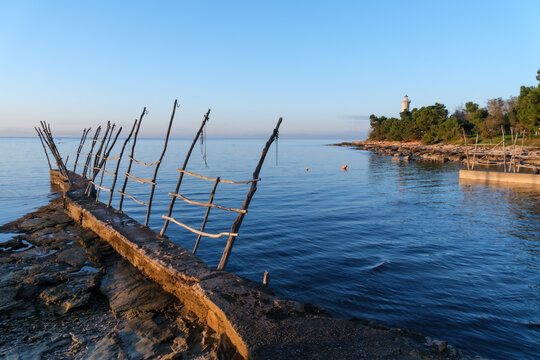 Wooden pier and lighthouse by the calm sea at sunset.