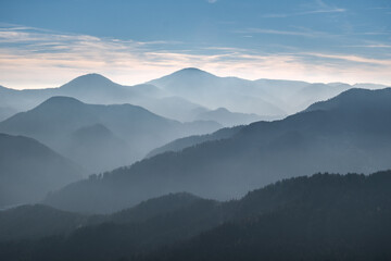 Misty mountain layers under a soft blue sky.