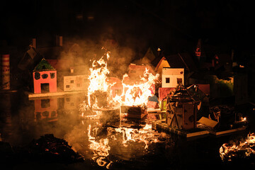 Miniature houses burn in a dark, smoky scene.
