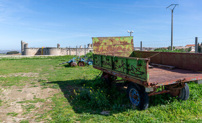 In the fields of the old medieval castle Castillo de los Condes, in Chinchón, Spain, there is an abandon and rusty old pick up bed from a truck, with the old castle in the background