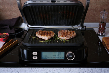 A marbled beef steaks grilling on an electric grill against the backdrop of a home kitchen.