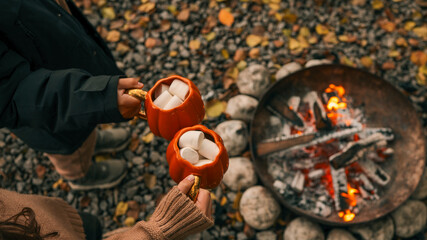 Cozy autumn scene with marshmallows in pumpkin mugs by a campfire