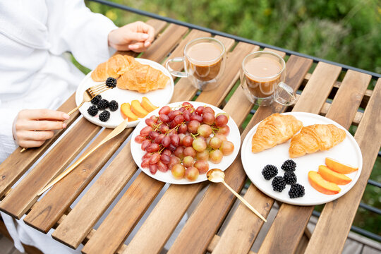 Delicious breakfast with croissants, fruits, and coffee served outdoors on a wooden table. Morning relaxation and healthy start of the day.